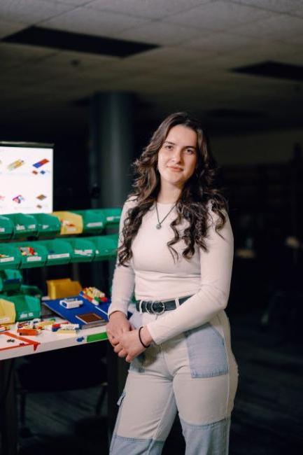 Kettering student Samantha Kneebone stands in the Lego Lab. A monitor shows Lego designs and containers hold colorful bricks.