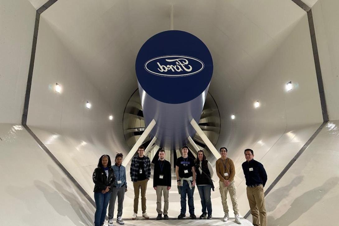 A group of eight individuals stand underneath a Ford logo