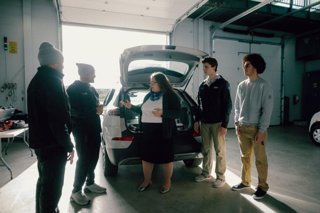 A group of people stand around the back of a car with the trunk hatch open